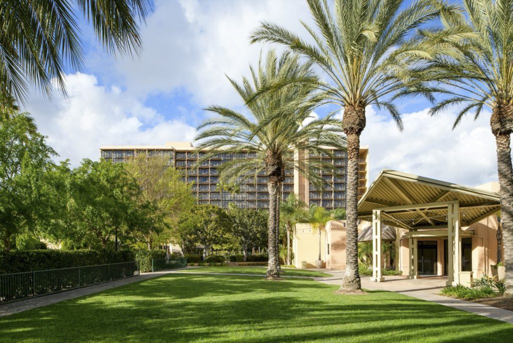 Exterior of the conference hotel with lawn and palm trees.